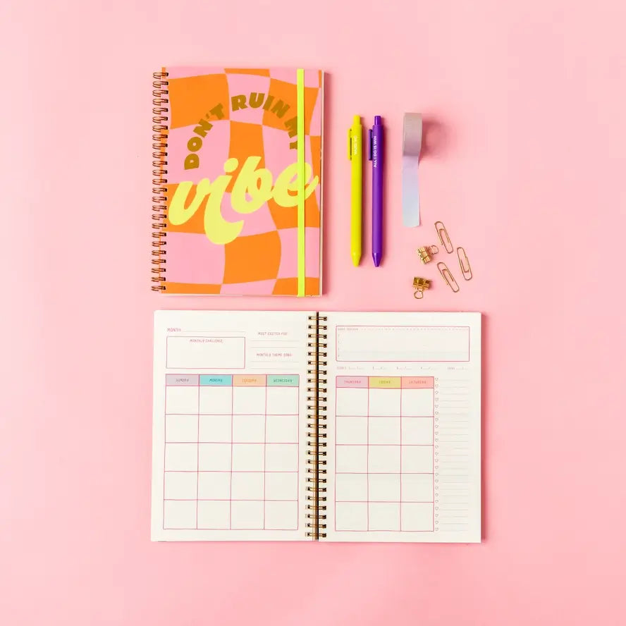 The colorful Don't Ruin My Vibe Small Goal Getter Lite closed, displayed above an open planner.