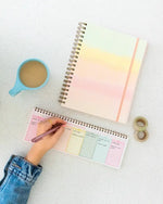 Someone writes in the Fresh Start Weekly Deskpad Planner, which sits next to the Daybreak Undated Perpetual Planner.