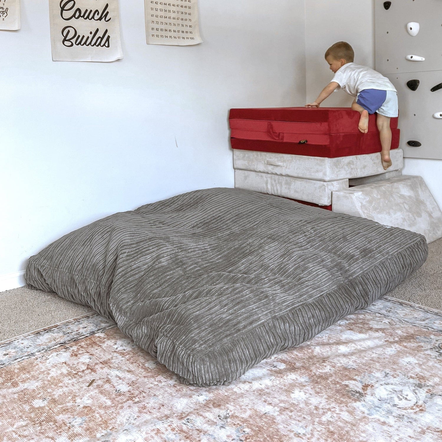 A child climbs on top of a soft tower positioned next to the Terry Corduroy Children's Sensory Crash Pad.