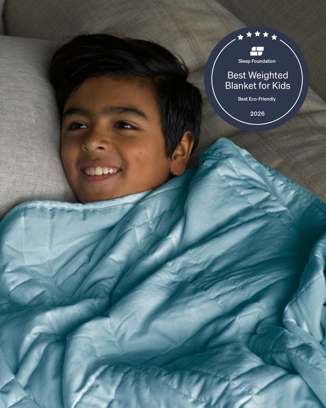 A child pulls the Aqua Mini Baloo Weighted Blanket up to their chin.