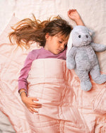 A child lays next to a stuffy under the Petal Pink Baloo Mini Weighted Blanket.