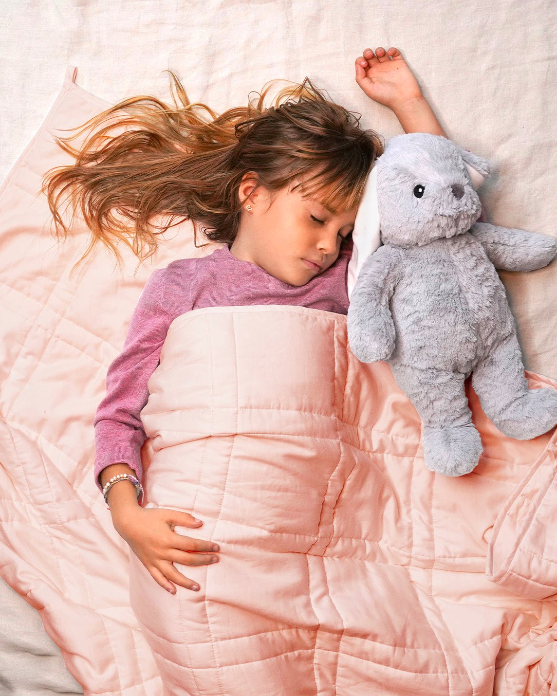 A child lays next to a stuffy under the Petal Pink Baloo Mini Weighted Blanket.