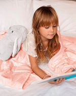 A child reads while under the Petal Pink Baloo Mini Weighted Blanket.