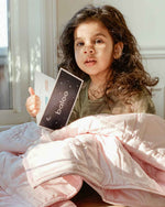A child holds the information card for the Petal Pink Baloo Mini Weighted Blanket.
