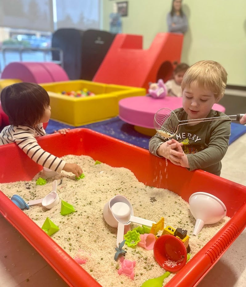 two toddlers playing in a bin of rice with toys
