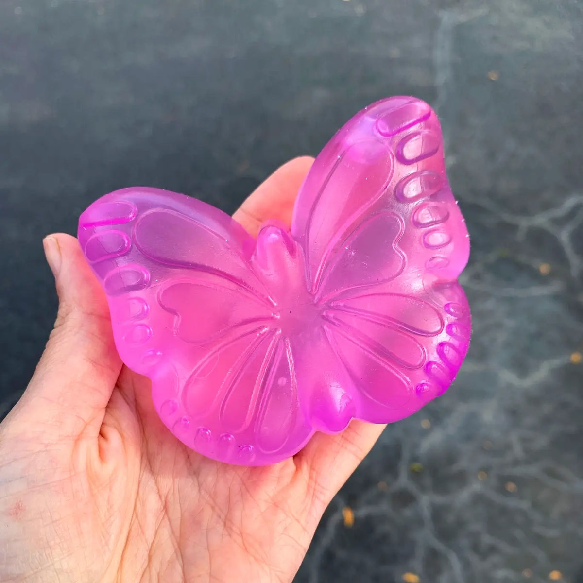 A hand holds the pink  Super Duper Sugar Squisher Butterfly.