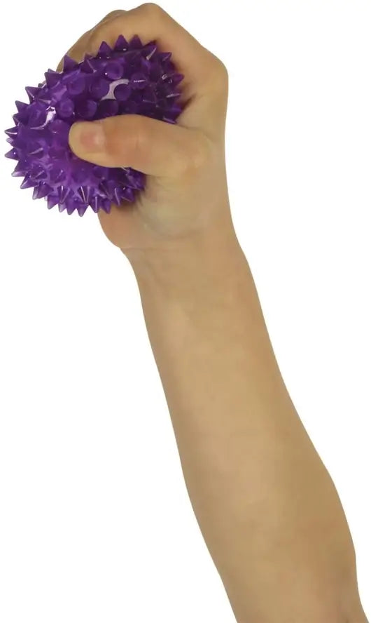 A child's hand holds up a purple Spiky Light Up Bouncy Ball while squishing it.