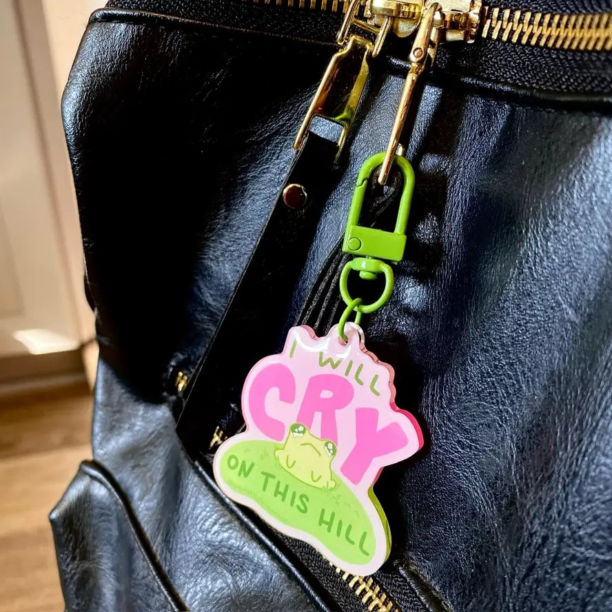 The "I Will Cry On This Hill" Keychain attached to a leather bag's zipper.