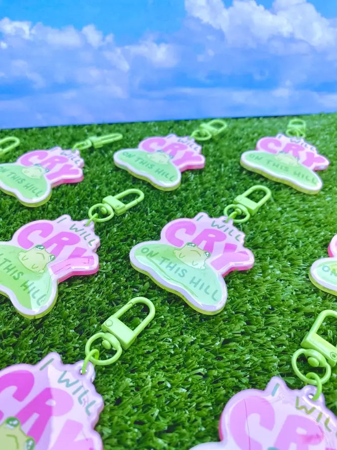 Many "I Will Die on This Hill" keychains are in a non-descript formation over fake grass.