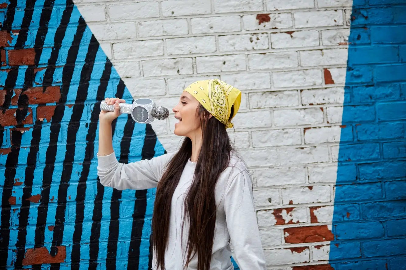 A woman with a yellow bandana sings into the Silver Bling Karaoke Mic & Bluetooth Speaker.
