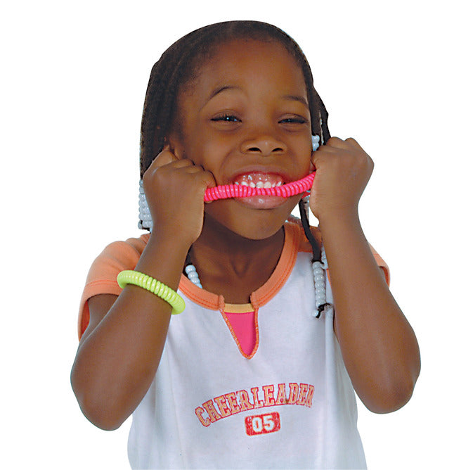 A child with dark skin tone and box braids with white beads is chewing on a pink Abilitations Chewelry Chewable Necklace.