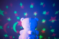 The backside of a Lumipets Sound Soother Bear sitting in front of the projection of stars coming from the display on its stomach.