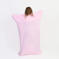 A child with long brown hair pulled into a ponytail on top of their head is facing away from the camera while in the Pink Body Sock. They are stretching out their limbs to create a sheet effect.