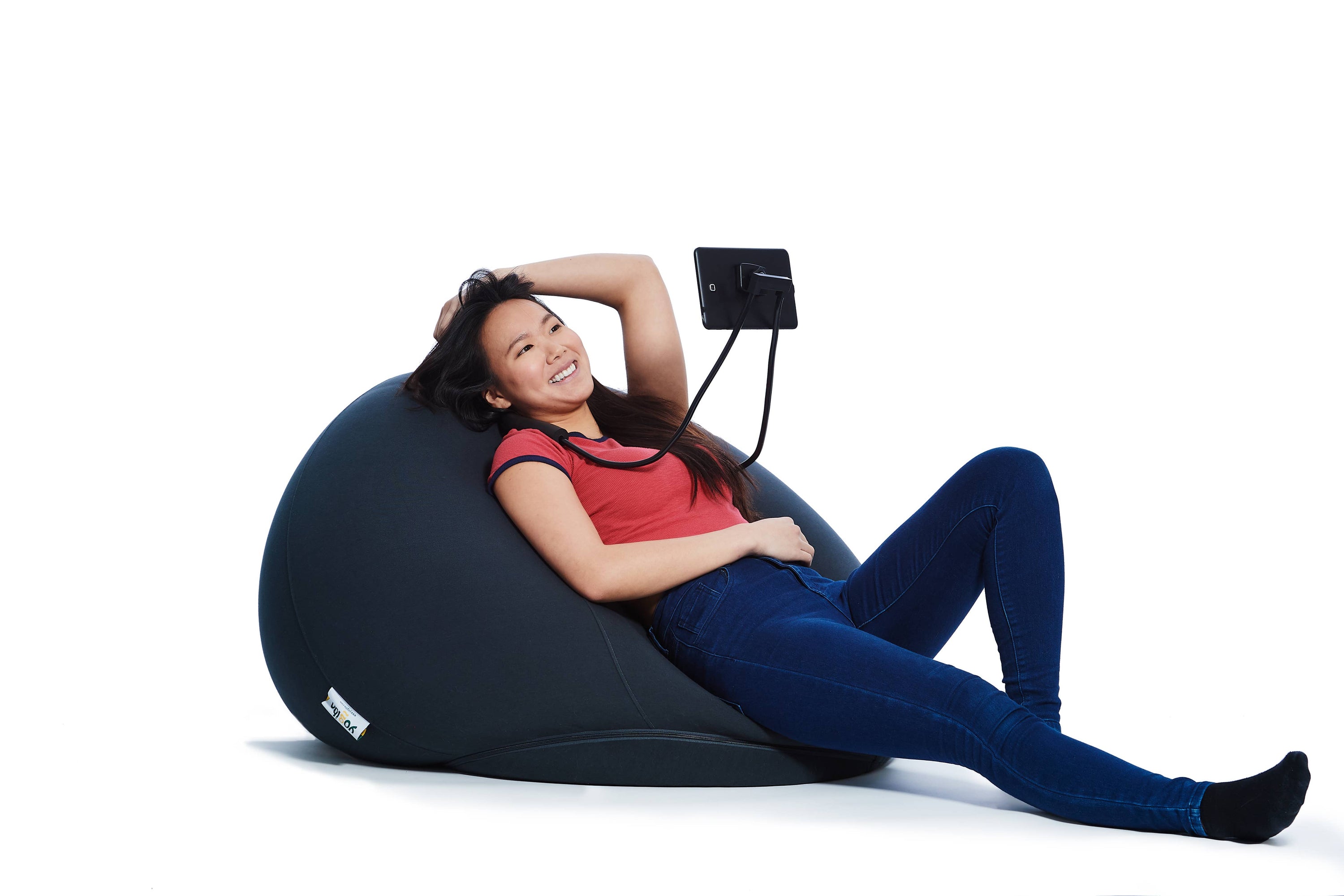 A person with medium light skin tone and long dark hair relaxes on a Yogibo while wearing a Grippibo Hands Free Device Holder.