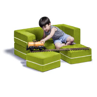 A child with light skin tone and short black hair is sitting on the loveseat portion of the Jaxx Zipline Modular Kids Loveseat and Ottomans. The ottomans are sitting in front of the loveseat on the floor, and a toy train track runs across the both of them. The child is holding a toy train piece on the edge of the track.