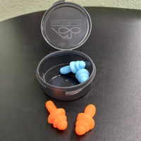The Sensory Tool House Limited Edition Noise Reducing Ear Plugs case is open and the blue pair of ear plugs is inside. The orange pair is sitting in front of the case.