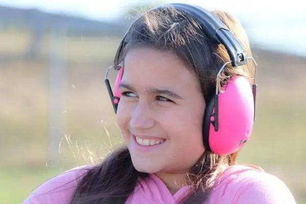 A child with light skin tone and long brown hair is wearing the Hot Pink Kids Earmuffs and smiling.