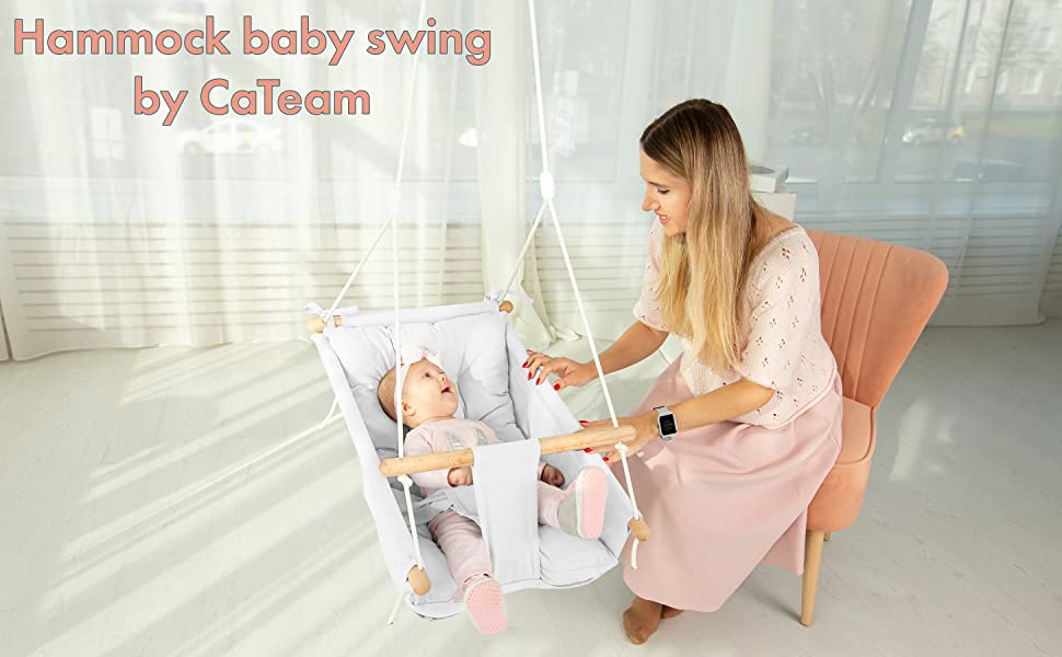 A baby with light skin tone lays back in the Canvas Baby Hammock Swing. The baby is smiling up at an adult with light skin tone and long blonde hair, who is sitting next to and looking down at the baby.