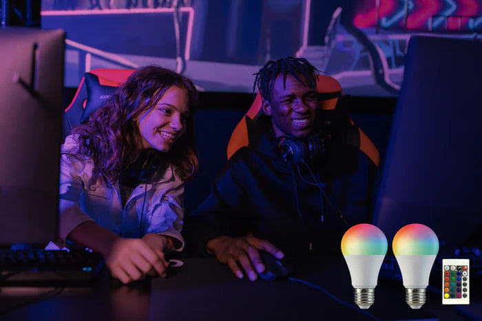 Two people sit in front of computer monitors, gaming, while an ambient light is on in the background.