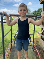 A child with light skin tone and blonde hair wears a black Sensory Compression Shirt and a pair of jean shorts on an outside play structure.