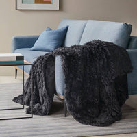 A fuzzy black weighted blanket is thrown over the side of a blue couch.