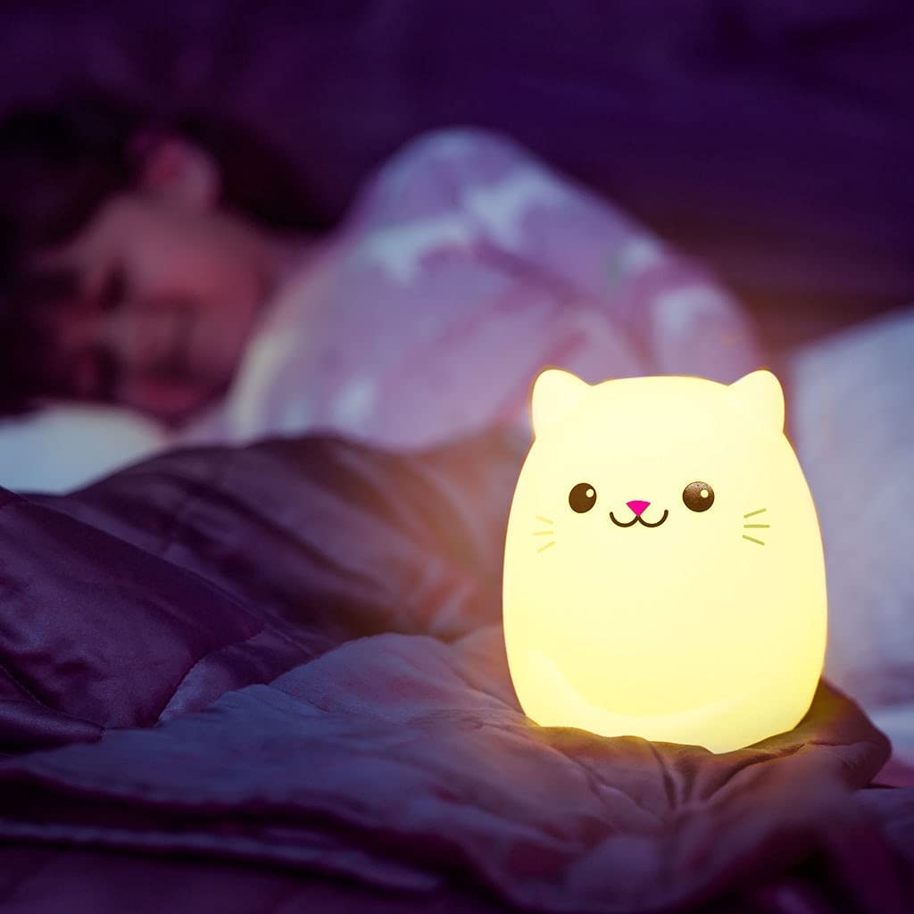 A Cat LED Night Light Bluetooth Speaker is lit up in the foreground. Behind it is a child under the covers.