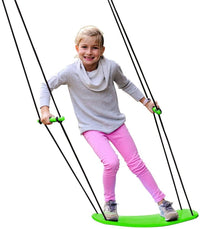 A child with light skin tone and blonde hair stands on the green Swurfer Kick. They are holding onto the two handles and leaning sideways, as if manipulating the board.