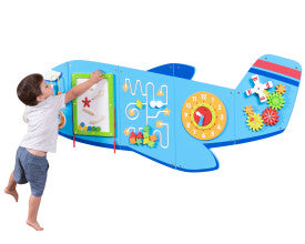 A child with light skin tone and short brown hair reaches towards one of the puzzles on the Airplane Activity Wall Panel.