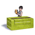 A child with light skin tone and short black hair is standing on the far side of the Jaxx Zipline Modular Kids Loveseat and Ottomans. They are holding a toy train piece, and there is a set of tracks running scross the length of the loveseat.