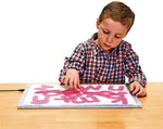 A child with light skin tone and short brown hair sits at a desk with a light table. Their hand is posed over SiliShapes Trace Alphabet letters.