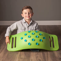 A child with light skin tone and short brown hair is kneeling on the floor and holding a green Teeter Popper on its side. The suction cups are displayed.