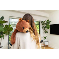 A person with long brown hair is holding the Bear Hugimals Weighted Stuffed Animal. The Bears head is peaking over their left shoulder.