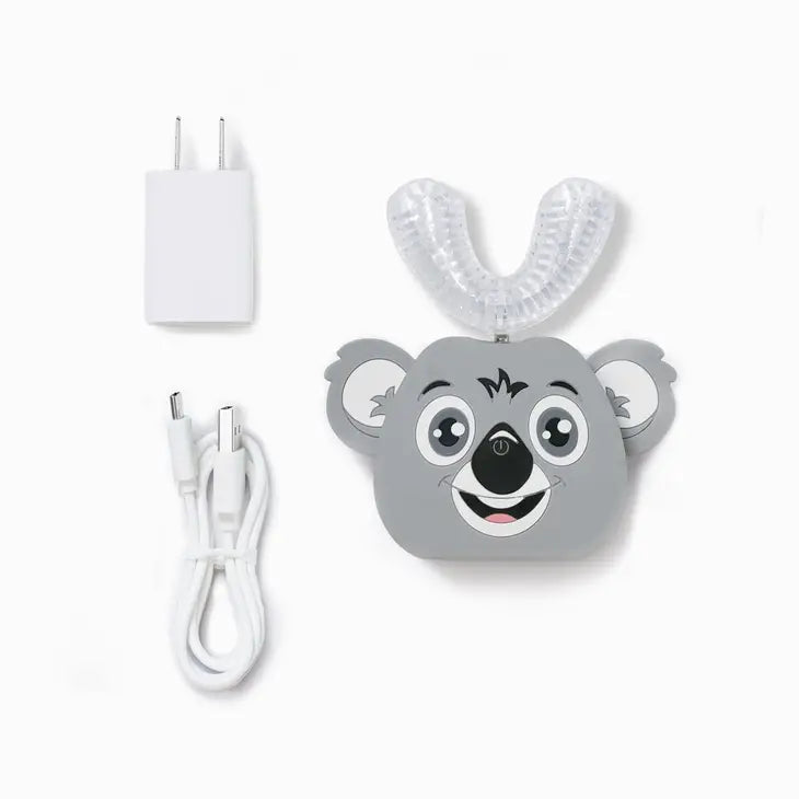 The Koala AutoBrush Pro Kids next to the charging cable and adapter that comes with it.