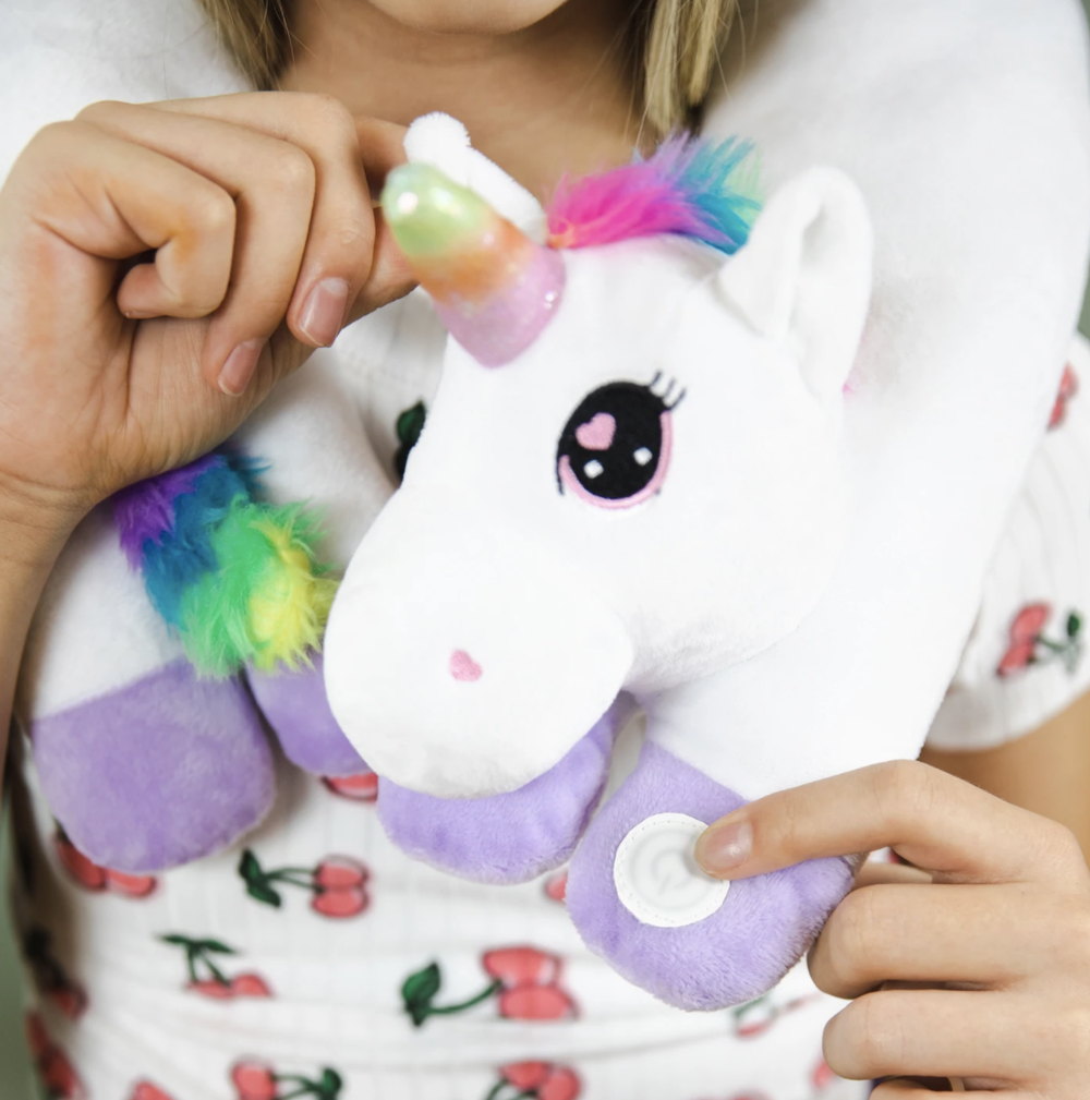 A child with light skin tone and long blonde hair wears a Unicorn Vibrating Neck pillow around their neck.
