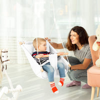 A toddler leans back in the Hammock Swing looking to an adult on its left. The adult is kneeling and has their hand on the top portion of the swing.