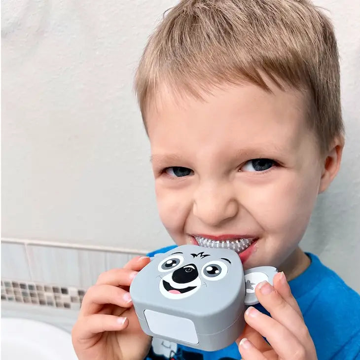 A child with light skine tone and short blonde hair has the Koala AutoBrush Pro Kids in their mouth and is holding it up using the ears.