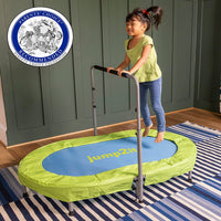 A child with medium skin tone and long brown hair worn up in pigtails is holding onto the handlebars of the Jump2It Trampoline and in mid-air. There is a seal for the Parents Choice Recommendations Award won by the trampoline.