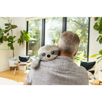 A person with short grey hair is holding the Sloth Hugimals Weighted Stuffed Animal over their left shoulder.