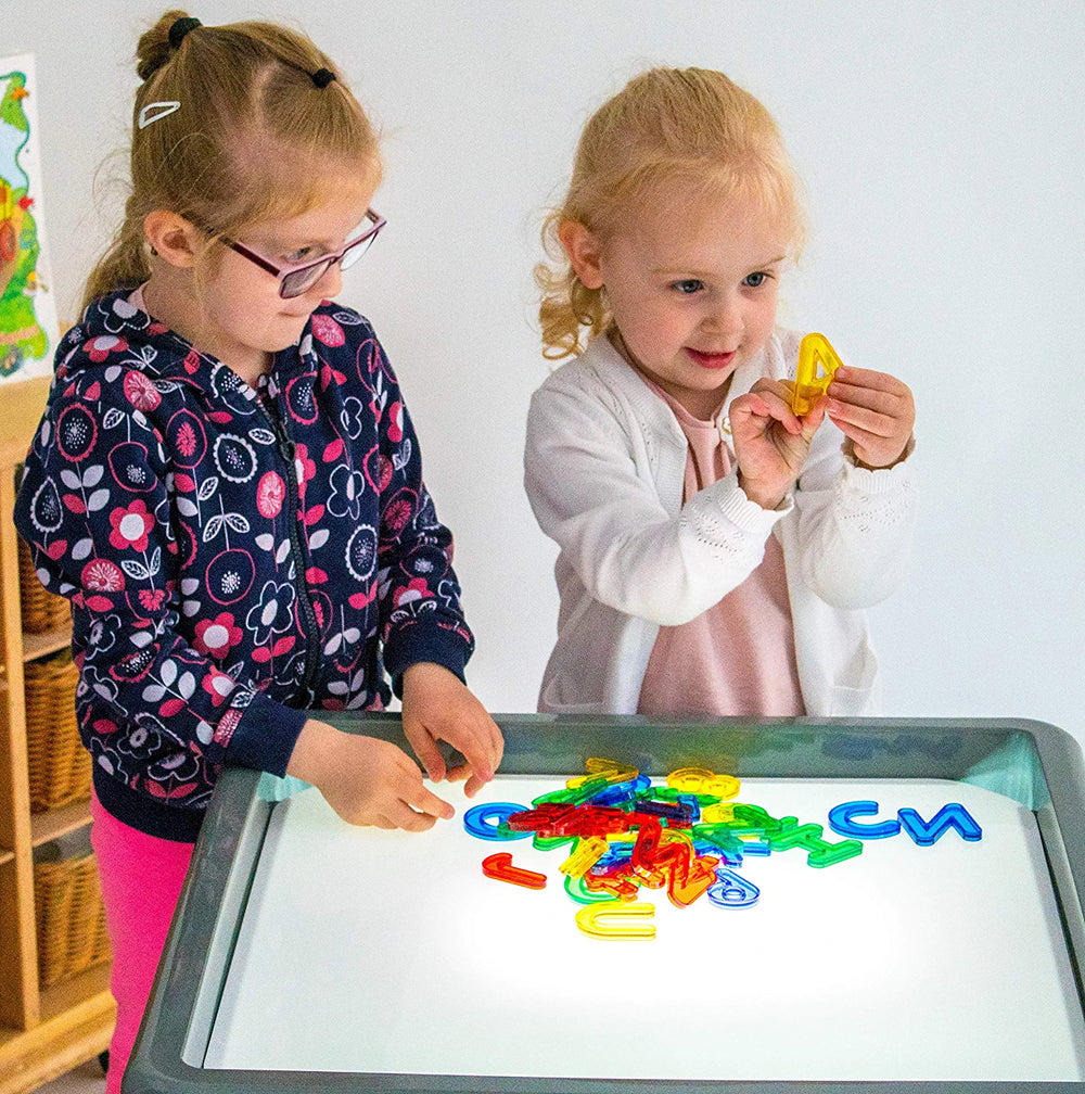 Two children stand over a light box with a pile of the Transparent Letters and Numbers.