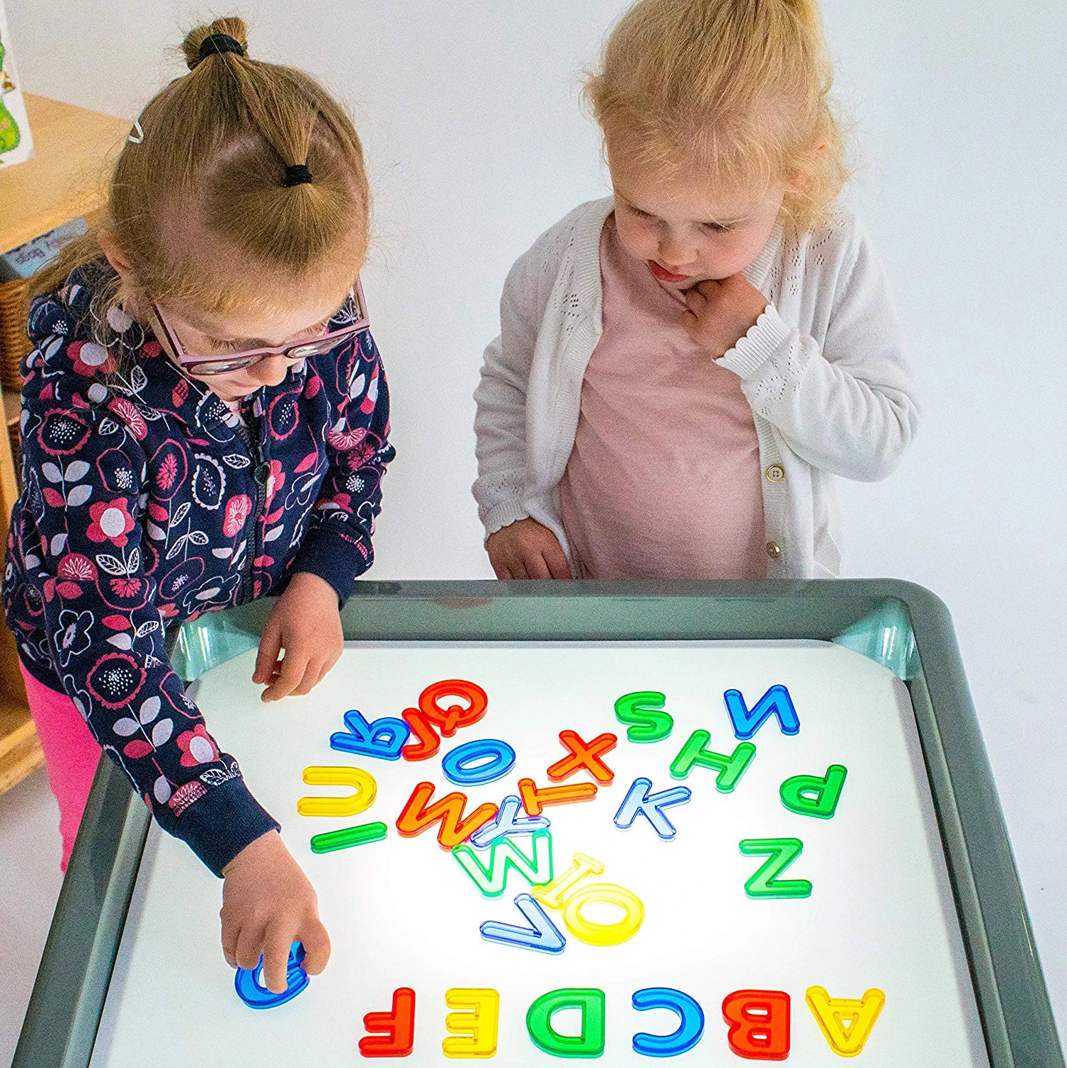 Two children stand over a light box and organize pieces of the Transparent Letters and Numbers.