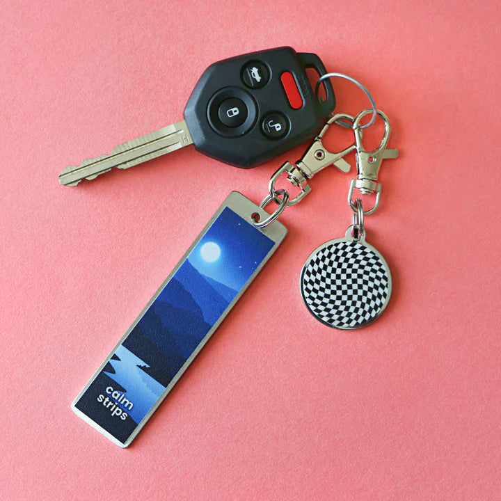 A keychain with a car key, a Calm Strip on a Carry Tag, and a black and white tchotchke.