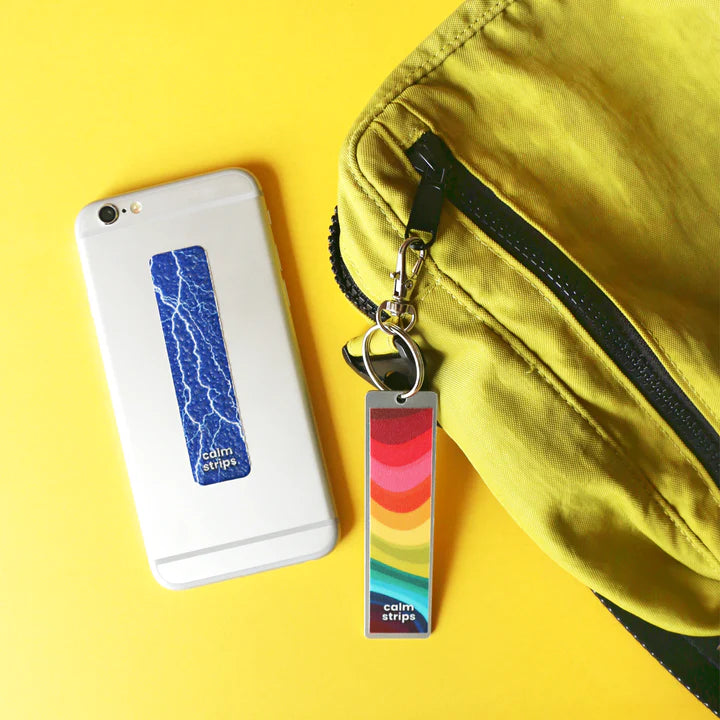 The Summer Storm Calm Strip is on the back of a white cell phone, and another unspecified Calm Strip is on a keyring attached to a bag.