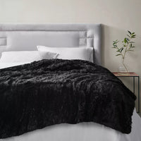 The Weighted Blanket Shaggy Fur Throw is thrown over the end of a bed.