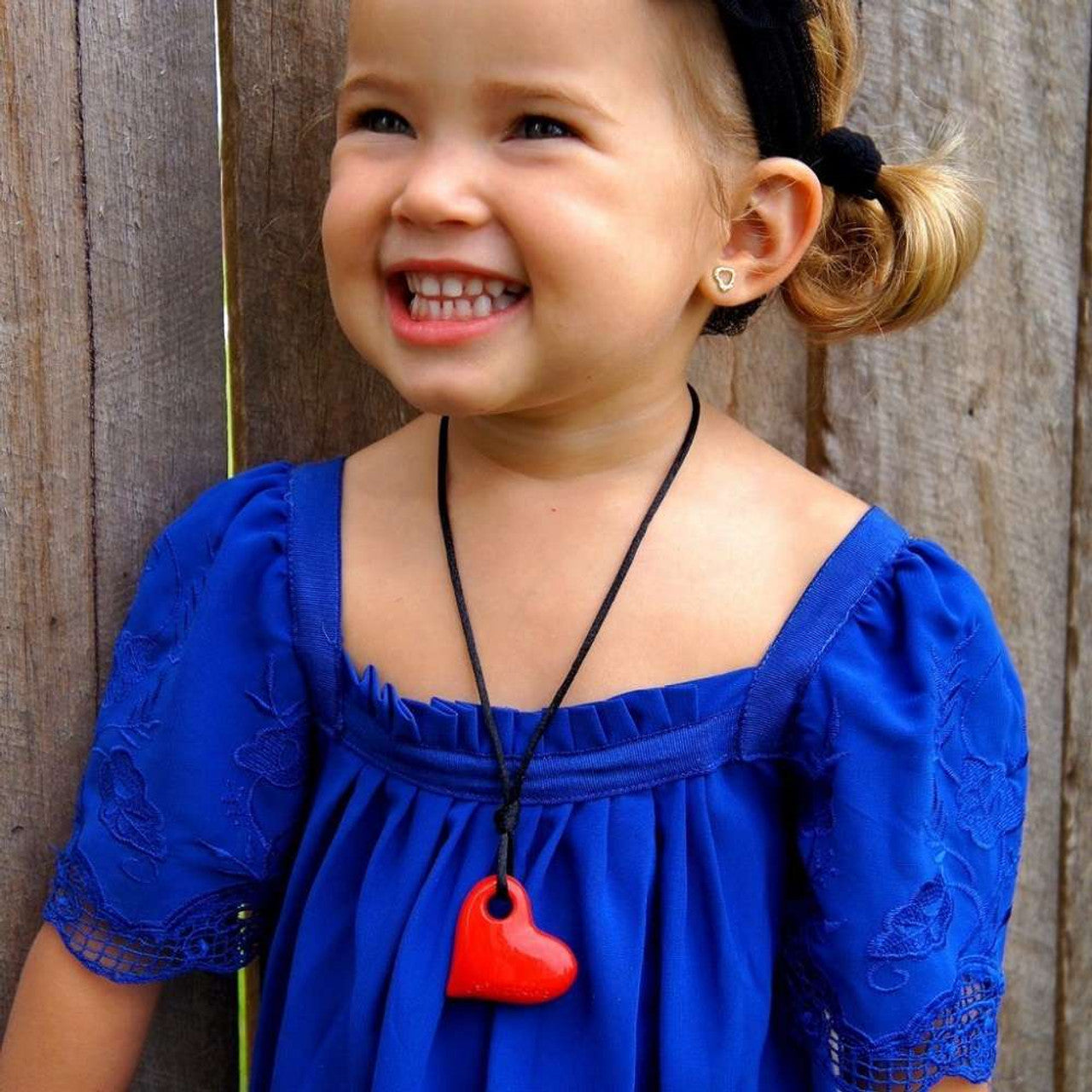 A child wtih light skin tone and blonde pigtails is smiling and wearing a red Heart Pendant.