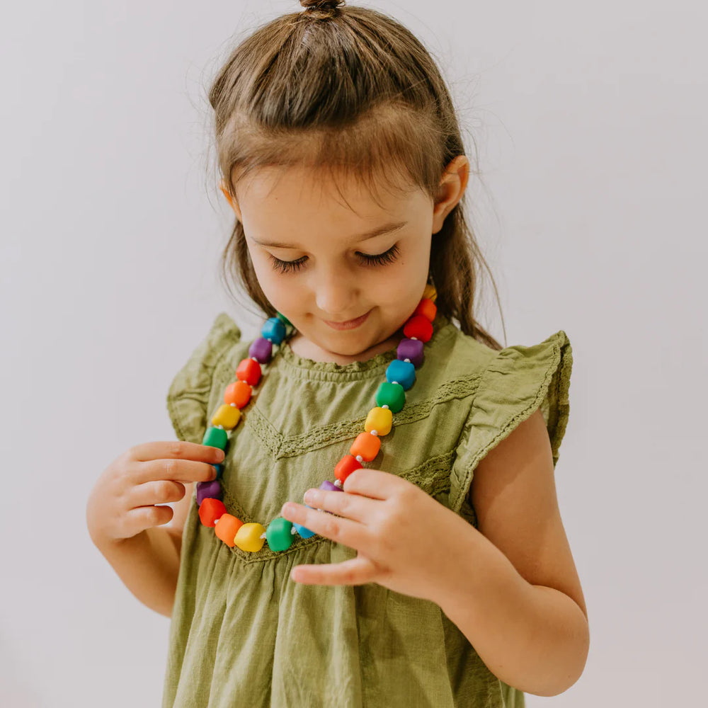 A child with light skin tone and long brown hair is looking down at the Princess and the Pea Necklace around their neck.