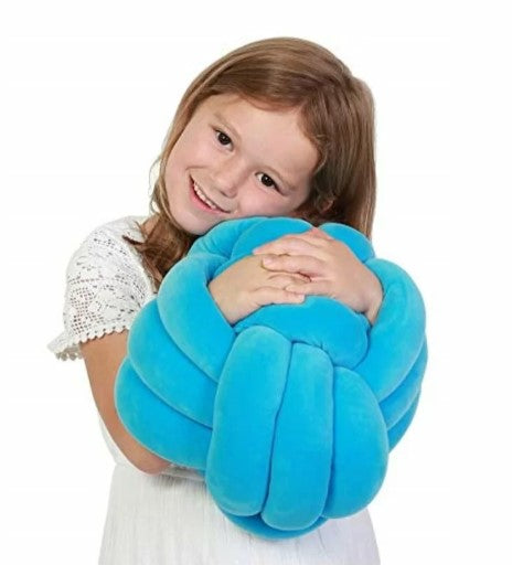 A child with light skin tone and brown hair puts her arms through the knotted texture of the Cuddle Ball Sensory Pillow to hug it.