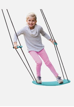 A child with light skin tone and blonde hair stands on the blue Swurfer Kick. They are holding onto the two handles and leaning sideways, as if manipulating the board.