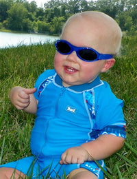A baby with light skin tone sits in the grass outside wearing lapis Bubzee Polarized Wrap Around glasses.