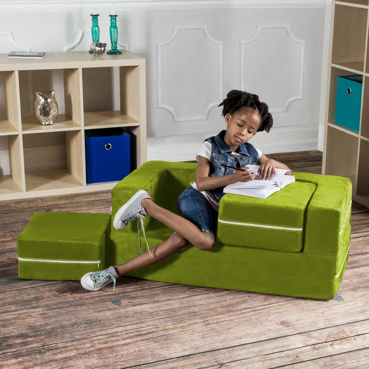 A child with dark skin tone and short black hair sits on the Lime Jaxx Zipline Modular Kids Loveseat and Ottomans. One of the cushions is on the floor next to the Loveseat and the other cushion is still in the Loveseat and being used as a desk.