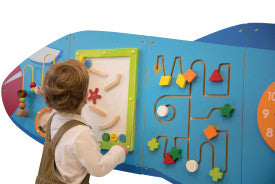 A child stands in front of one of the puzzle panels of the Airplane Activity Wall Panel.